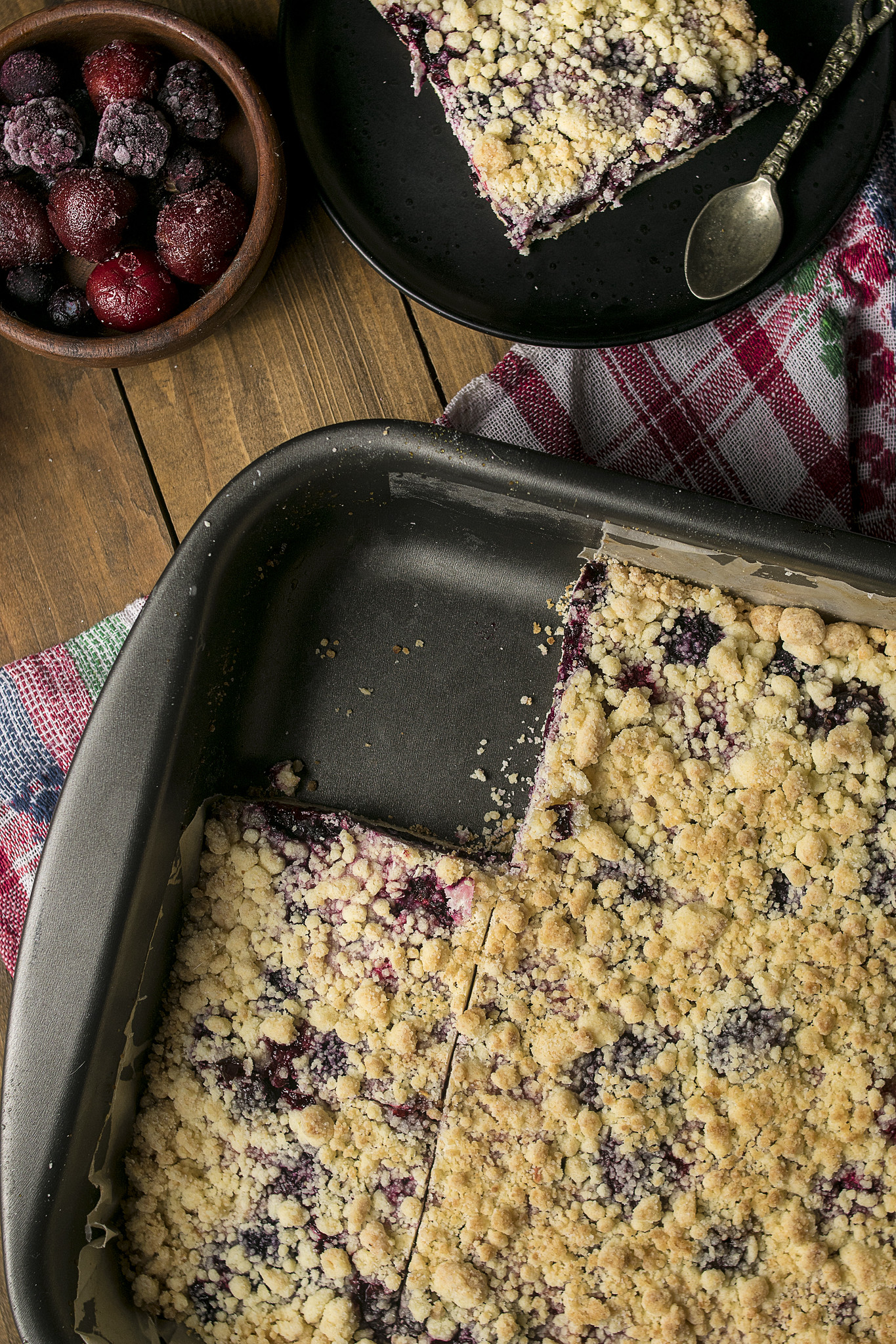 Baked rustic Italian berry crumble tart in a tin with slices cut, showing golden crumb topping and dark berry filling beneath.